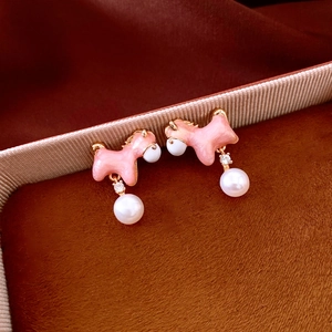 Detailed shot of pink enamel horse earrings with pearls on a textured ribbon