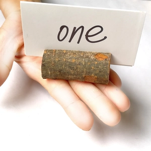 Hand holding a natural wood cylinder card holder with a handwritten 'one' note on white card