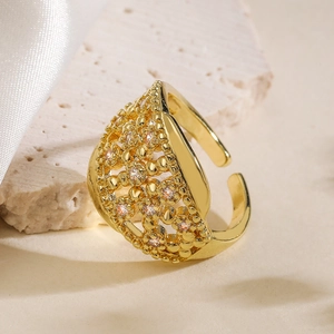 Golden hollow geometric open ring featuring white zircon stones on beige stone