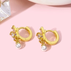 Détail de boucle d'oreille papillon dorée avec zircons roses et perle blanche sur fond rose