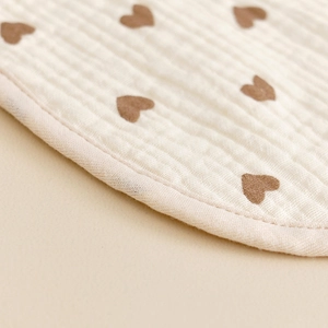 Close-up of soft cotton gauze baby bib featuring brown heart patterns and neat edging
