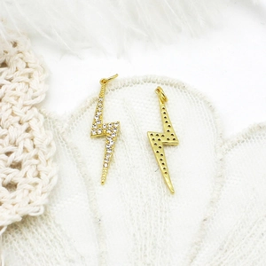 Detail of 18K gold-plated lightning pendants with crystals on lace and feather backdrop