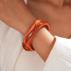 Macro detail of wide resin bangle in dark amber with marbled texture on model