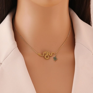 Golden snake pendant necklace with green crystals on a model wearing a beige blazer