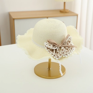 Detailaufnahme eines beigen Strohhutes mit Wellenrand und floraler Schleife mit Pompons