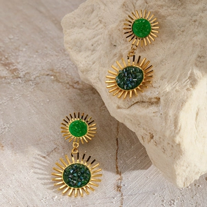 Detail shot of gold sunburst earrings with green crushed stone inlay on a natural stone base