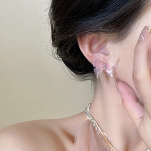 Gros plan d'une boucle d'oreille papillon rose avec ailes transparentes et dorures