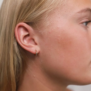 Detail of a rainbow gemstone hoop earring worn by a model in a luxury gold finish