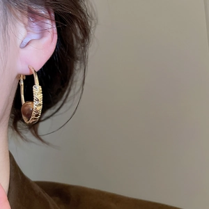 Detailed side view of a gold textured hoop earring with a brown bead on a female ear