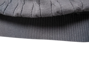 Macro shot of grey knit sweater showing detailed cable weave and ribbed cuff texture