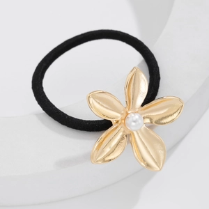 Close-up of golden flower hair tie with pearl center on minimalist white display stand