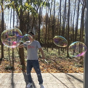 Outdoor long handle bubble wand creating giant colorful soap bubbles in a sunny forest park