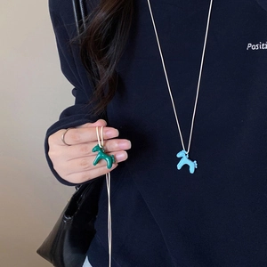 Macro detail of cute pony pendant necklace in green and blue on dark blue sweater
