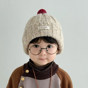 Detailaufnahme der Kinder-Strickmütze in Beige mit weichem dunkelrotem Bommel