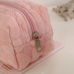 Detailed macro view of pink plush cosmetic bag with diamond quilted texture and silver zipper