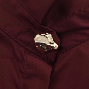 Detailed macro view of burgundy poplin fabric with a golden irregular lava metal button