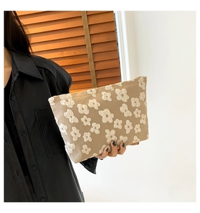 Detail of khaki fabric clutch bag featuring 3D white flower pattern held by a model