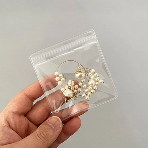 Transparent PVC storage bag holding gold hoop earrings with white faux pearls