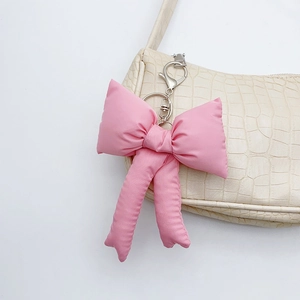 Chic pink fabric bow keychain with metal clasp hanging on a white textured bag