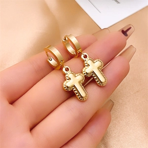 Polished gold stainless steel cross dangle earrings displayed on elegant champagne satin
