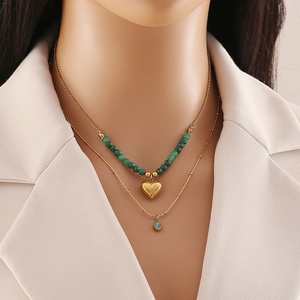Double-layered gold necklace with green beads, heart pendant and blue crystal on a model