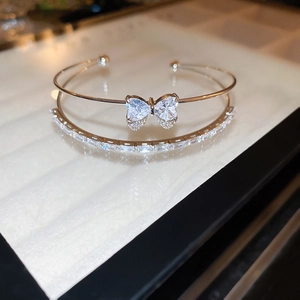 Detail of double-layer silver bangle featuring a zircon bow heart and tiered baguette crystals