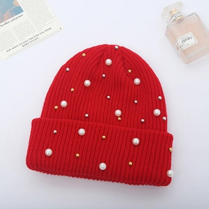 Detail of red cable knit beanie with faux pearls and metallic beads on white background