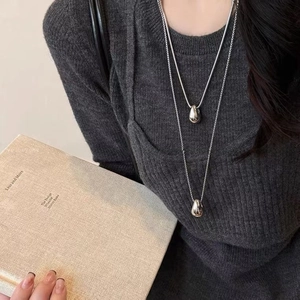 Close-up of double layer silver teardrop pendant necklace worn over a grey knit sweater