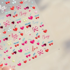 Close-up of 3D nail stickers featuring red cherries, pink bows, and crystal accents
