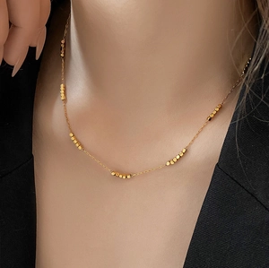 Detail of a minimalist gold beaded necklace on model highlighting fine metal textures