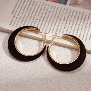 Macro detail of dark brown velvet circular earrings with gold metal hinges and soft textures