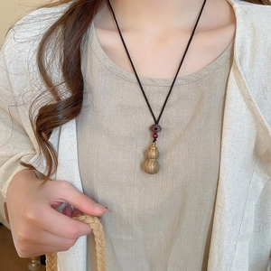 Detail of wooden gourd pendant with red agate bead and black cord on female model