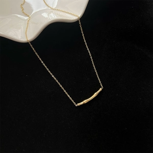 Gros plan d'un collier doré à barre incurvée sur un plat en céramique et fond noir