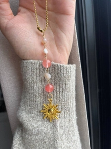 Detail of a golden sun pendant with colorful beads held against a grey sweater