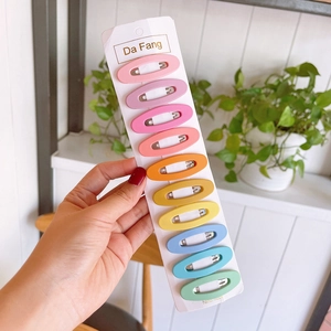 Set of 10 colorful matte oval snap hair clips on a white card with green plant background