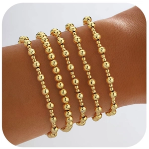 Dettaglio di cinque braccialetti con perline dorate sovrapposti indossati per un look boho