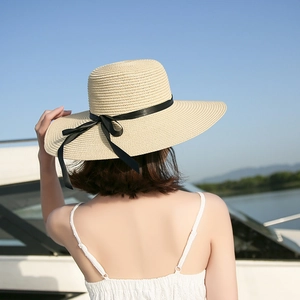 Detail of cream wide brim straw hat with black ribbon bow against a sunny lake background