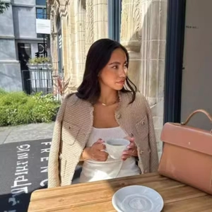 Women's beige tweed cropped jacket with gold buttons styled for an outdoor cafe setting