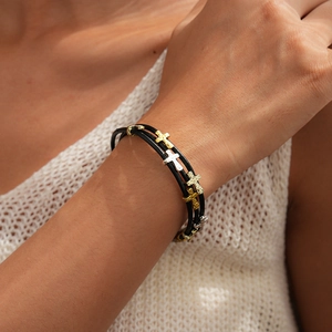 Gros plan d'un bracelet en cuir multicouche avec des breloques croix martelées dorées