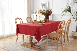 Detail of red cotton tablecloth featuring decorative white pom-pom lace edge on wood table