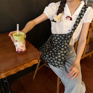 Green floral crossbody bag with heart pattern shown in a cozy cafe setting
