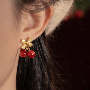 Detail of red cherry resin earrings with gold bowknot charm worn by a model