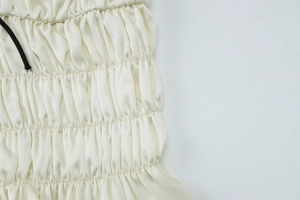 Macro shot of off-white satin fabric with elastic smocking and black drawstring detail