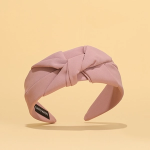 Close-up of pink pleated fabric headband with twisted knot design and handmade label