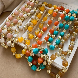 Detailed view of colorful acrylic beaded bracelets with irregular gold metal beads in a tray