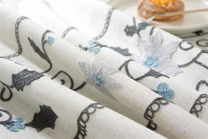 Detailed embroidery of blue flowers and grey leaves on beige linen blend tablecloth fabric