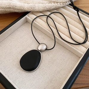 Détail du pendentif en bois ovale noir avec cadre argenté mat sur boîte à bijoux beige