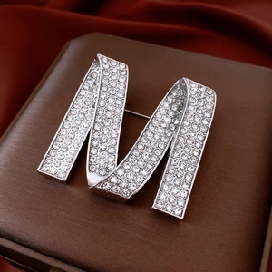 Détail de la broche lettre M argentée avec cristaux sur un coffret cadeau