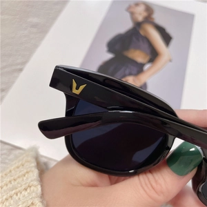 Close-up of black frame sunglasses with signature gold V-shaped metal temple detail