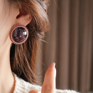 Macro shot of a purple resin earring with pink crystal border worn by a model